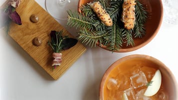 A wooden board with food items, a bowl of soup, and a glass of white wine on a table.