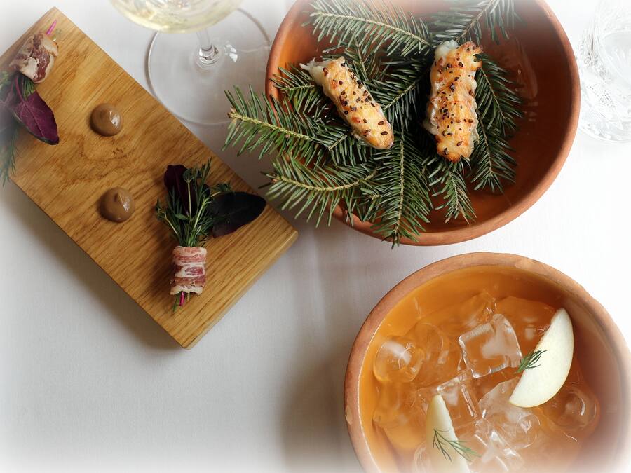 A wooden board with food items, a bowl of soup, and a glass of white wine on a table.