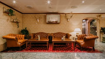 A lobby with a brick wall, a wooden sofa set, a red patterned rug, and a framed ship picture.