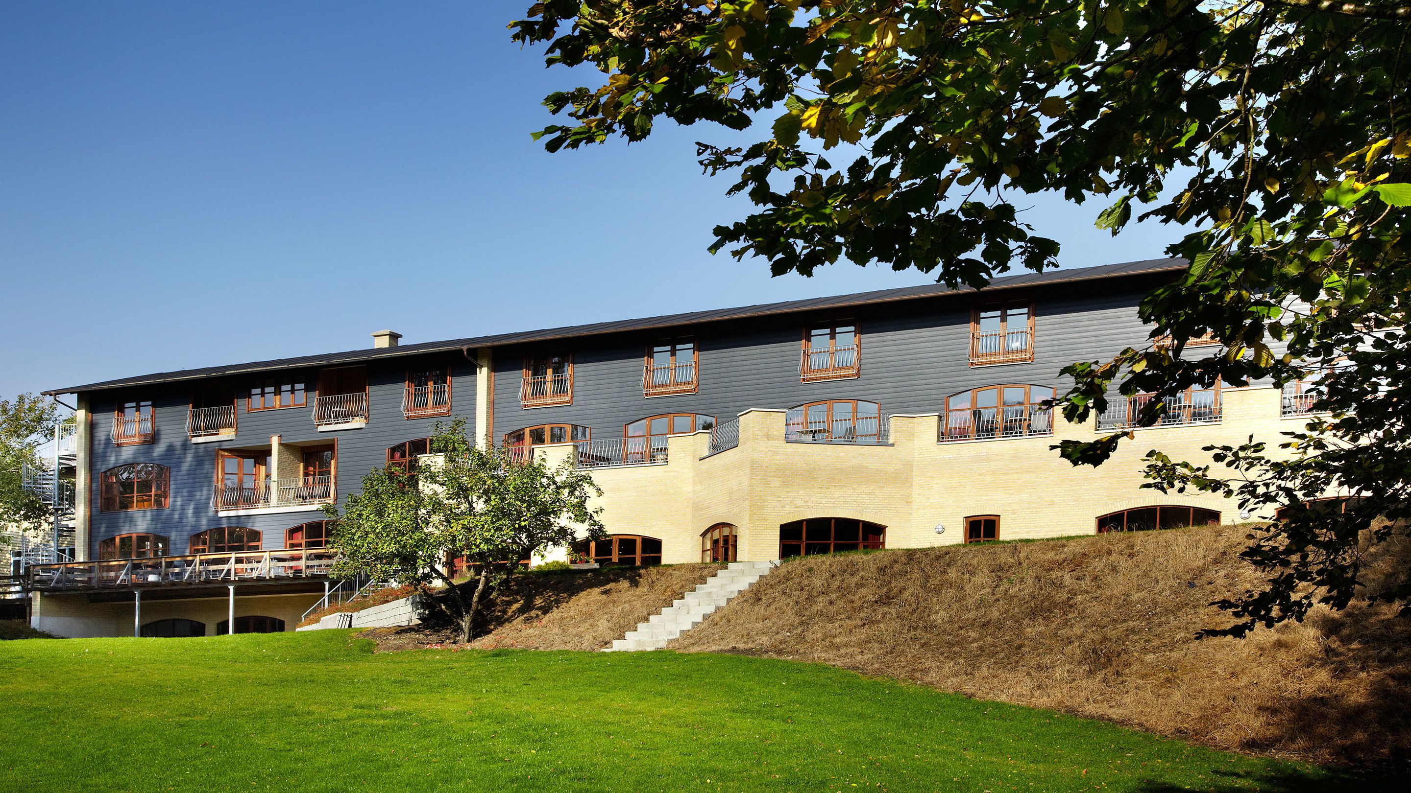 Ein mehrstöckiges Gebäude mit Flachdach, mehreren Balkonen und einer Treppe, die zum Eingang führt.