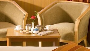 A hotel room with two armchairs, a small table with a vase and a book, and a bed with a striped pillow. - Ramanashree Brunton (Bengaluru)
