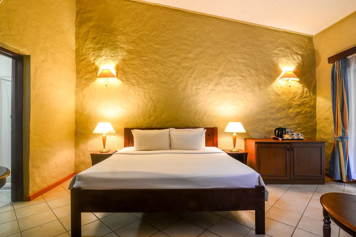 A hotel room with a large bed, two bedside lamps, a wooden nightstand, and a cabinet.