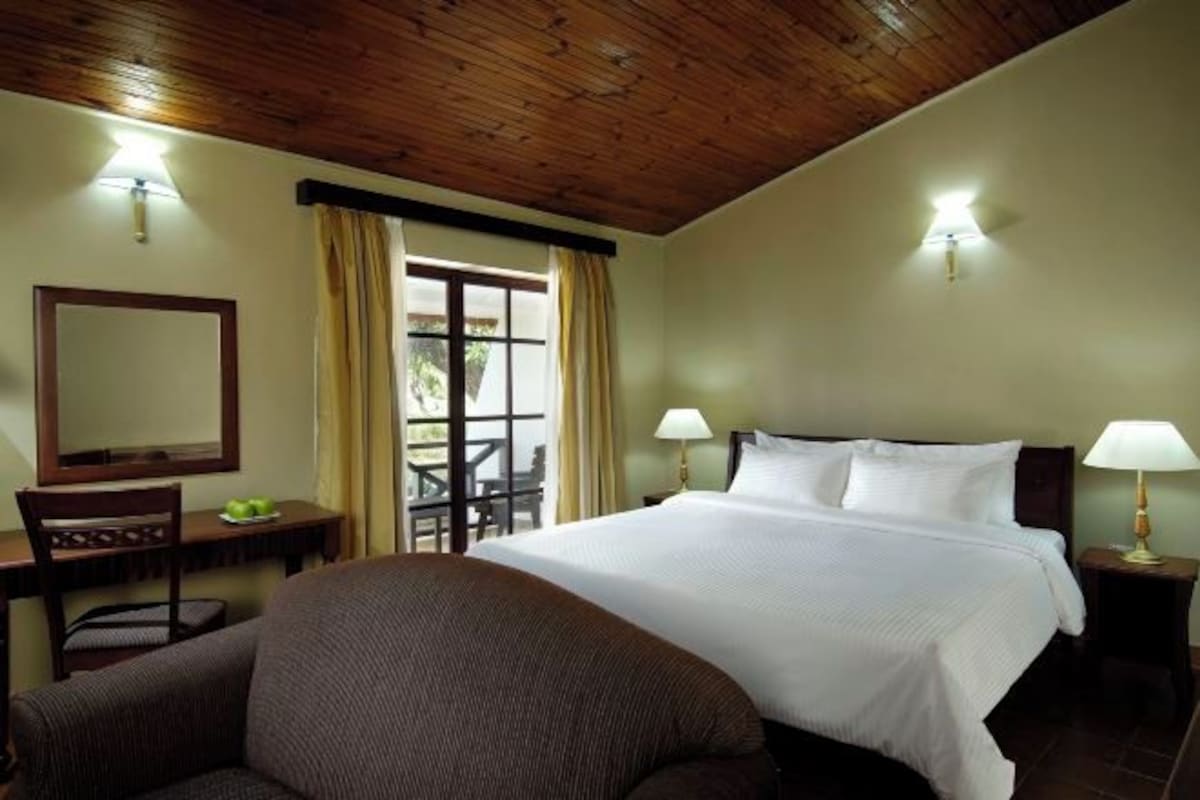 A hotel room with a bed, a desk, a chair, a mirror, and a window with curtains.
