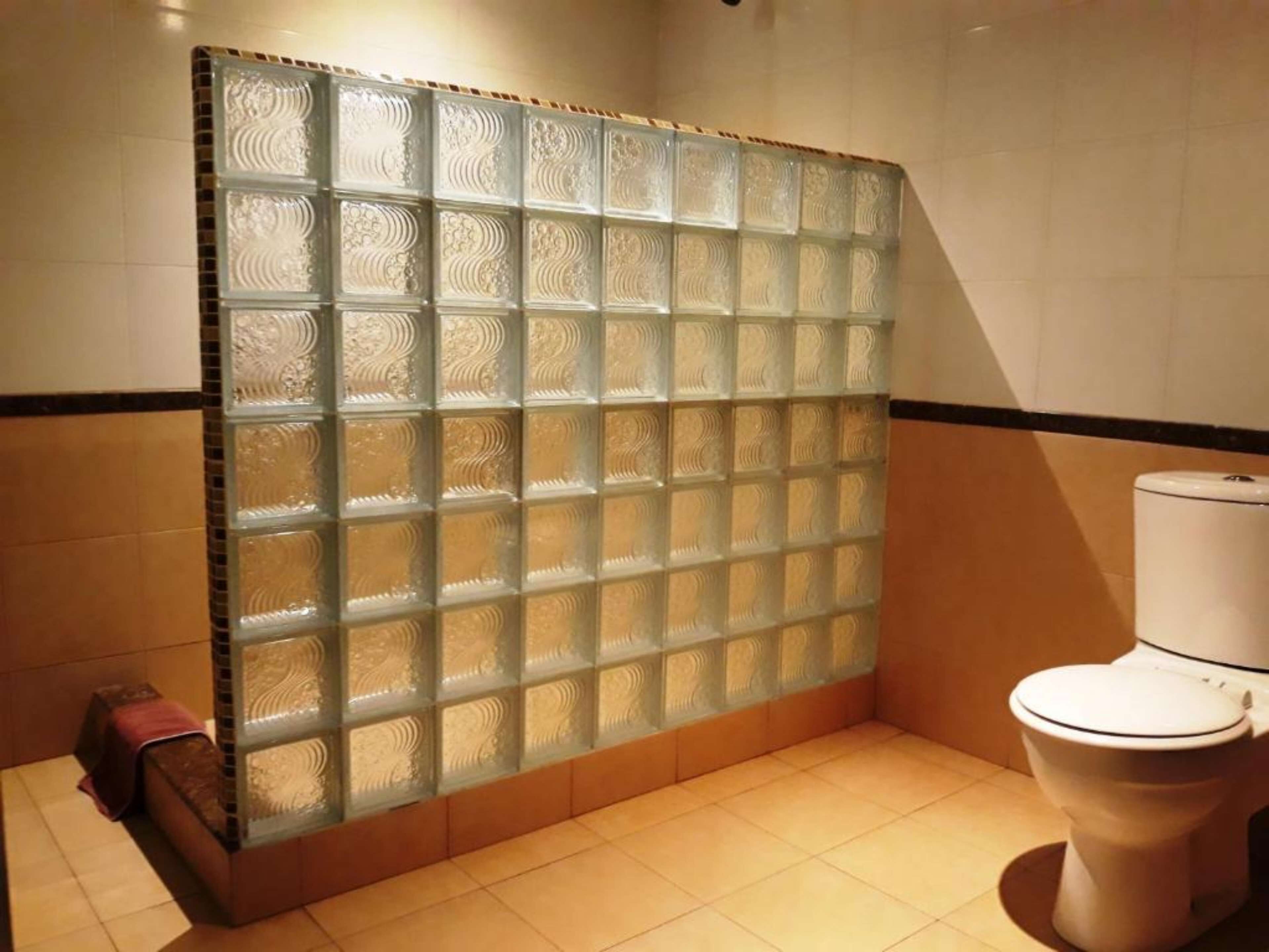 Casa de banho com cabine de chuveiro em vidro, sanita e paredes revestidas a azulejos.