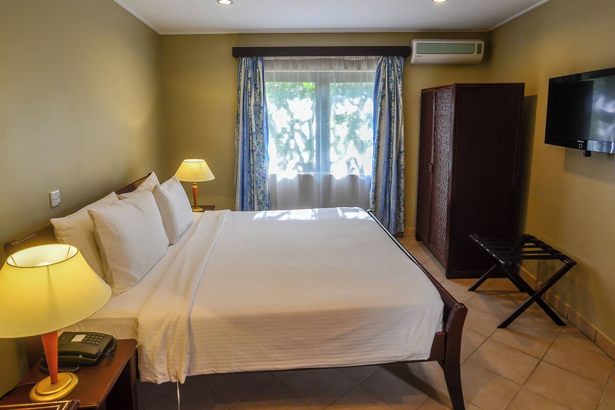A hotel room with a bed, bedside lamps, a telephone, an air conditioning unit, a television, and a wardrobe.