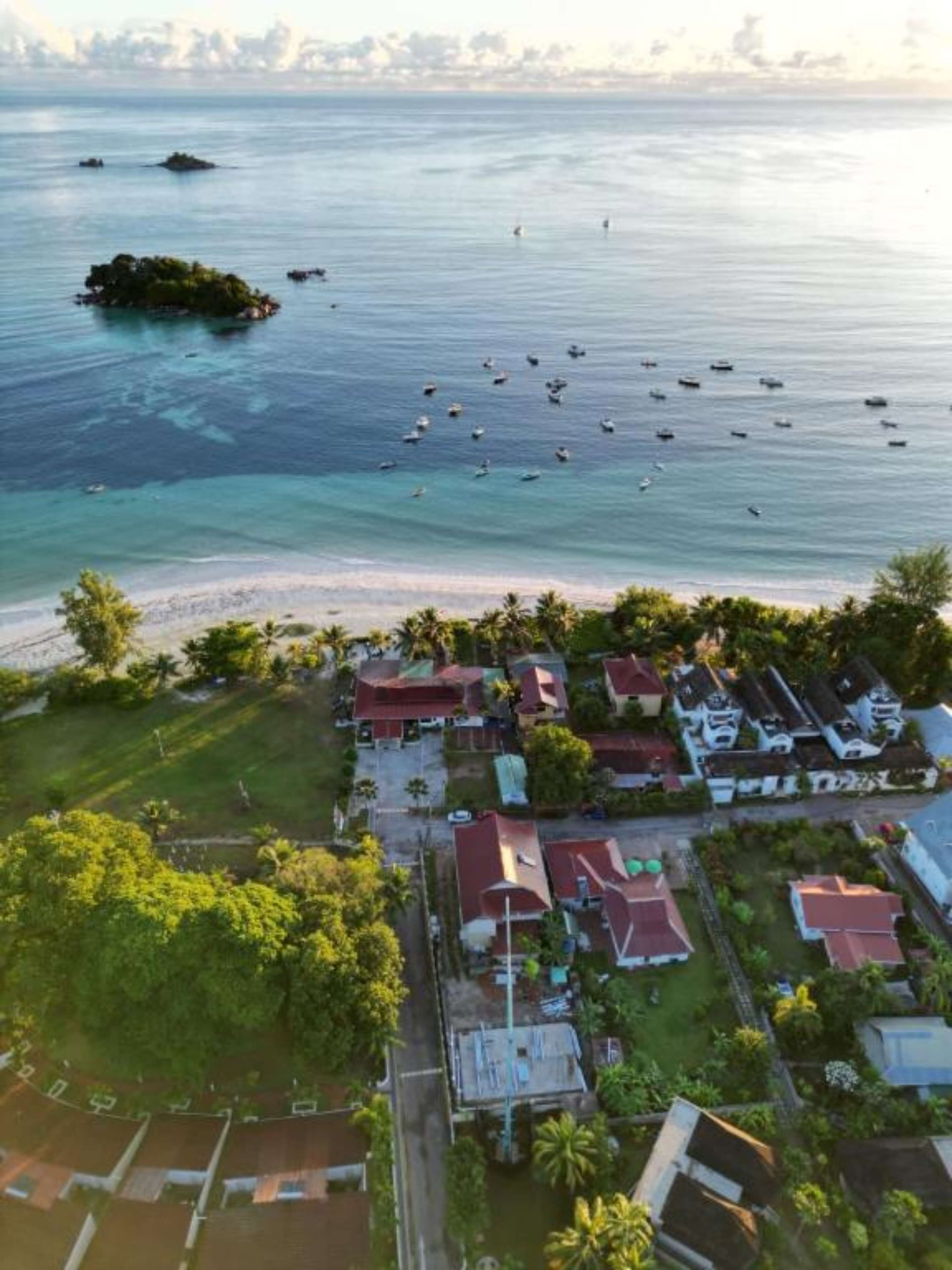 Vista aérea de una zona residencial costera con casas, una playa y barcos en el agua.