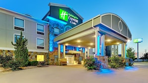 Un bâtiment Holiday Inn Express & Suites doté d’une façade en pierre, d’une entrée abritée et d’un éclairage extérieur soigné.