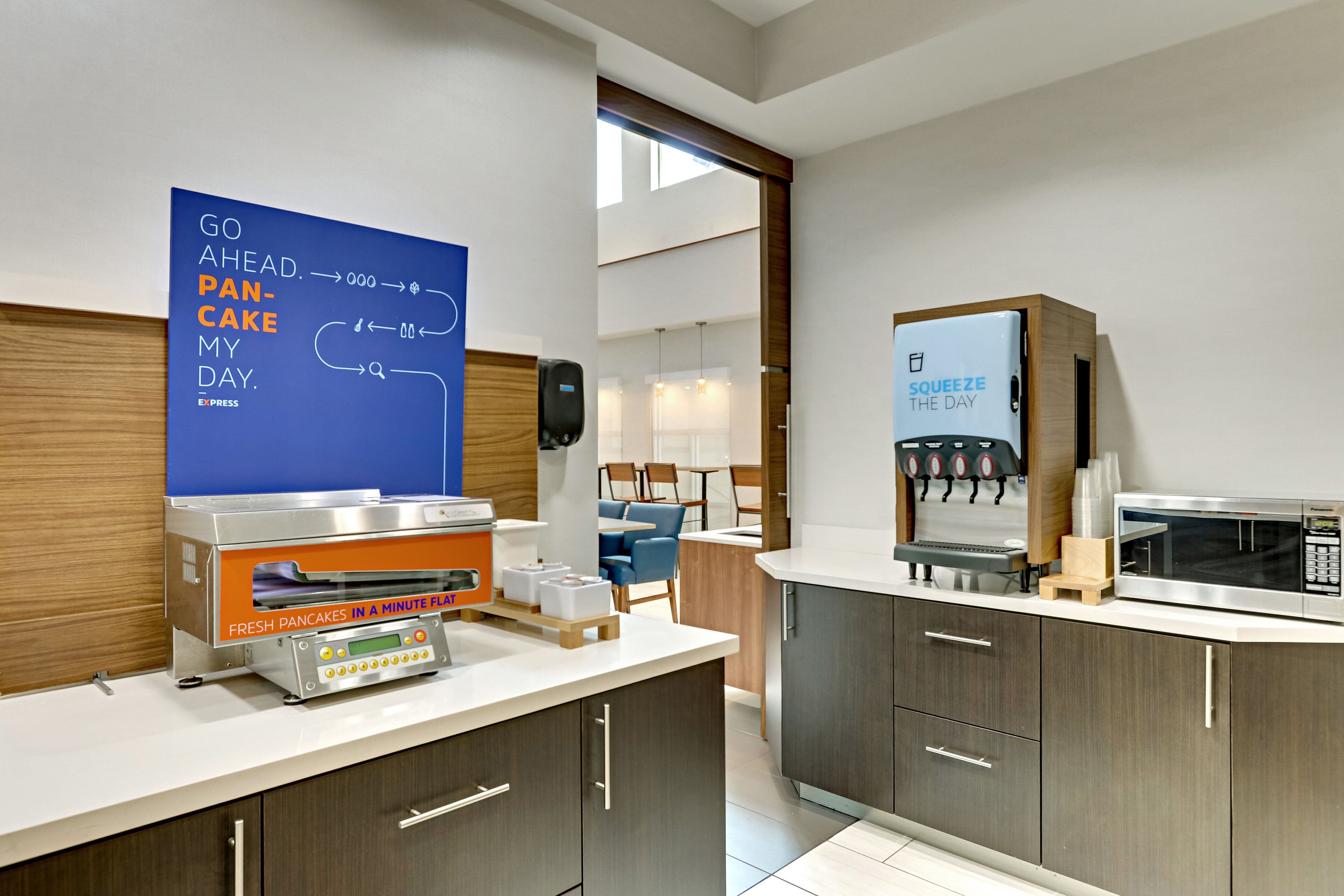 A modern kitchen with a fresh pancake machine, a microwave, and a sign encouraging guests to 'Go ahead, pancake my day.'