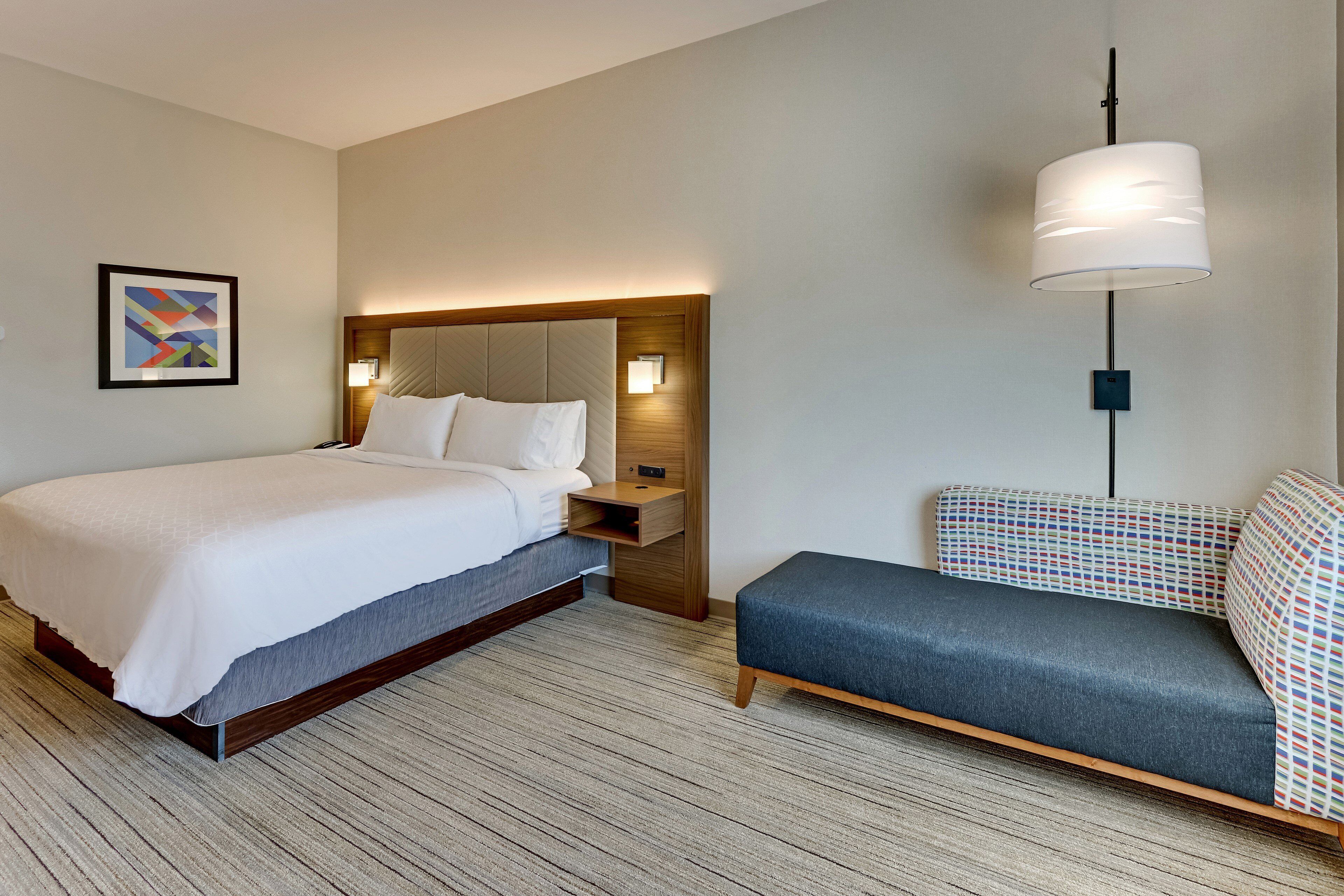 A hotel room with a bed, bedside table, lamp, and a sofa.