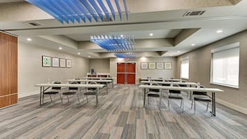 Un salón de conferencias con varias mesas y sillas, alfombra estampada y diseño de techo azul.