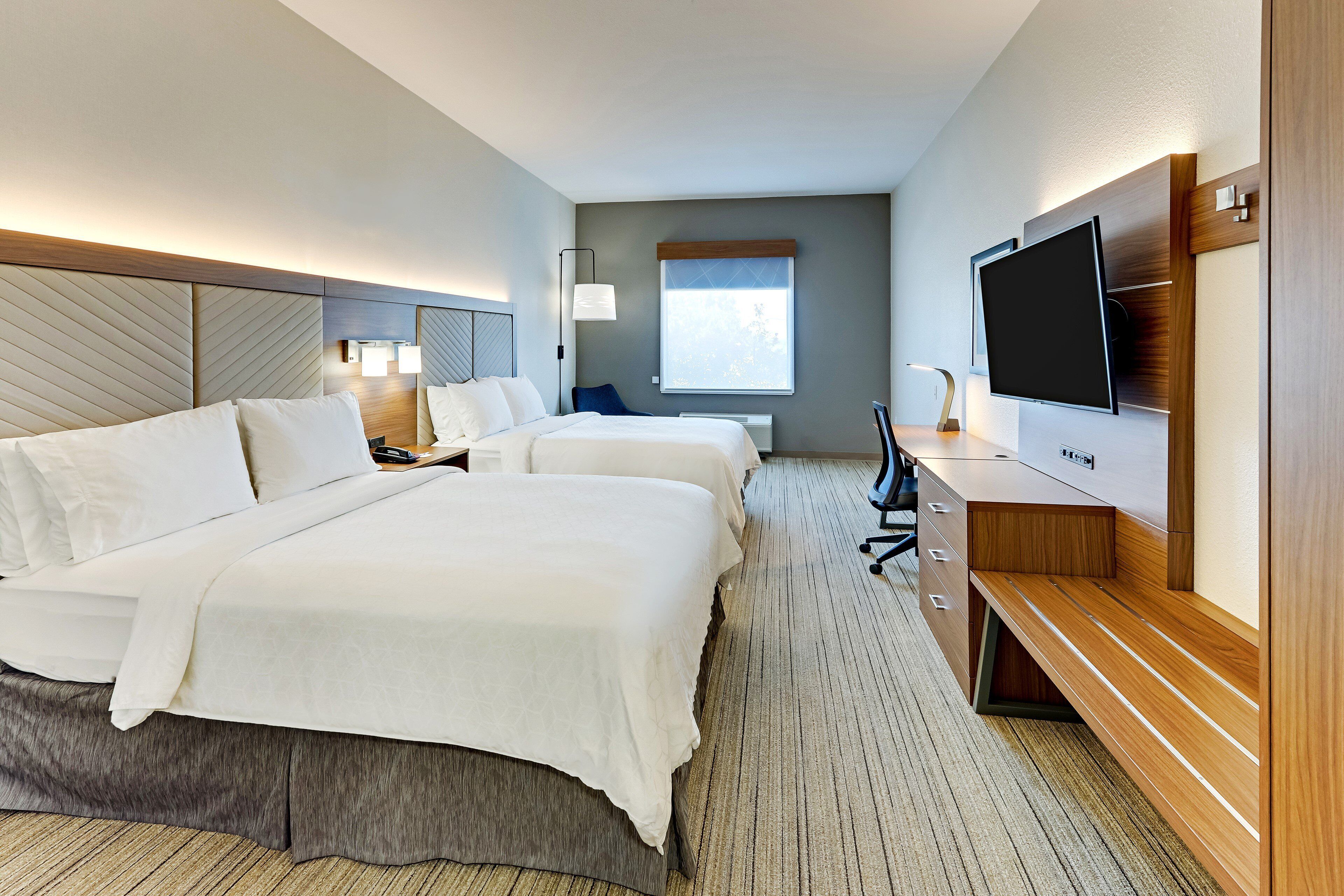 A hotel room with two beds, a TV, a desk, and a window.