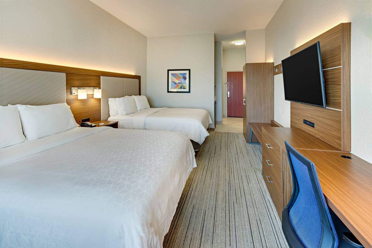A hotel room with two beds, a desk with a computer, a flat-screen TV, and a framed artwork on the wall.