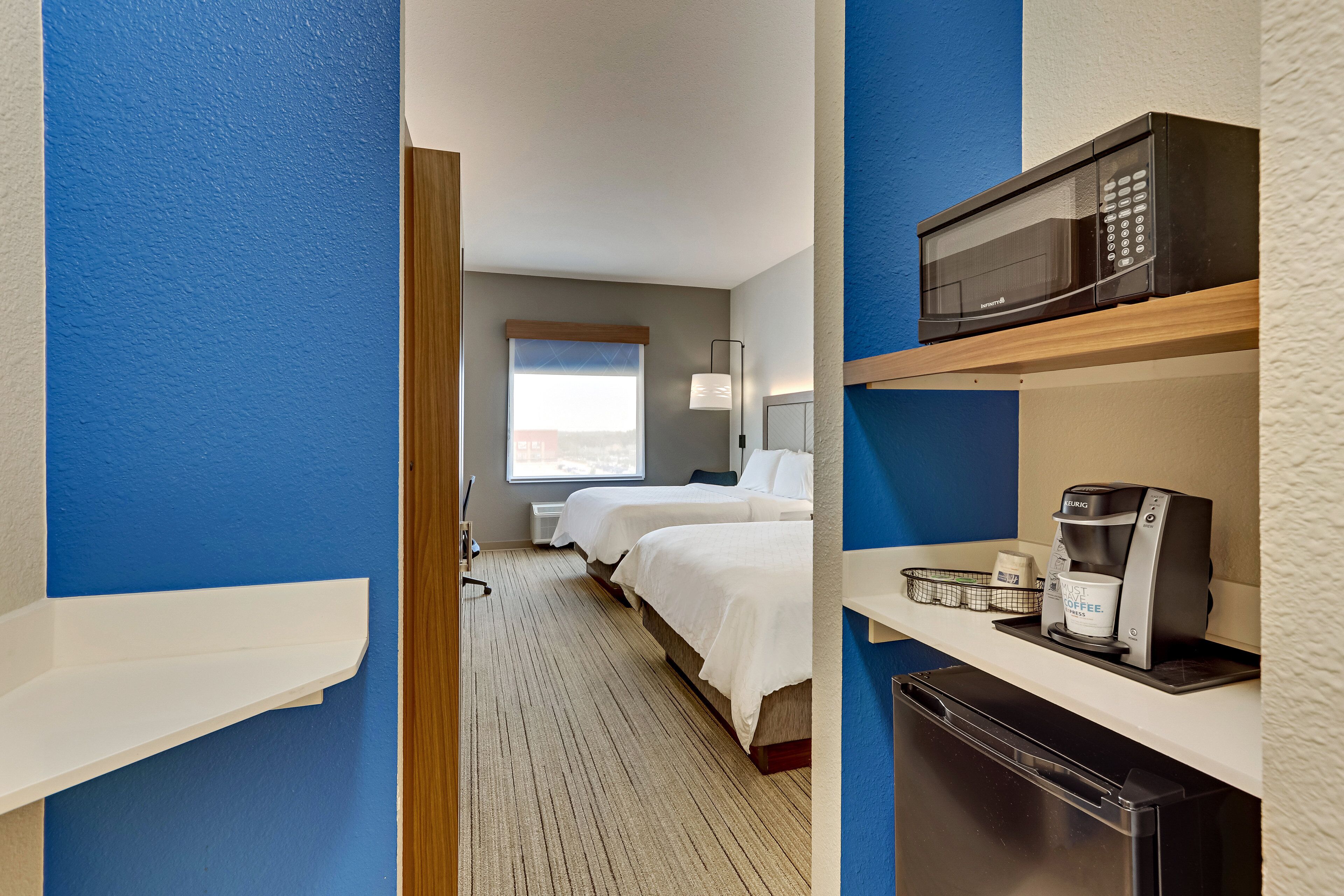 A hotel room with a bed, a microwave, a coffee maker, and a refrigerator.