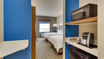 A hotel room with a bed, a microwave, a coffee maker, and a refrigerator.