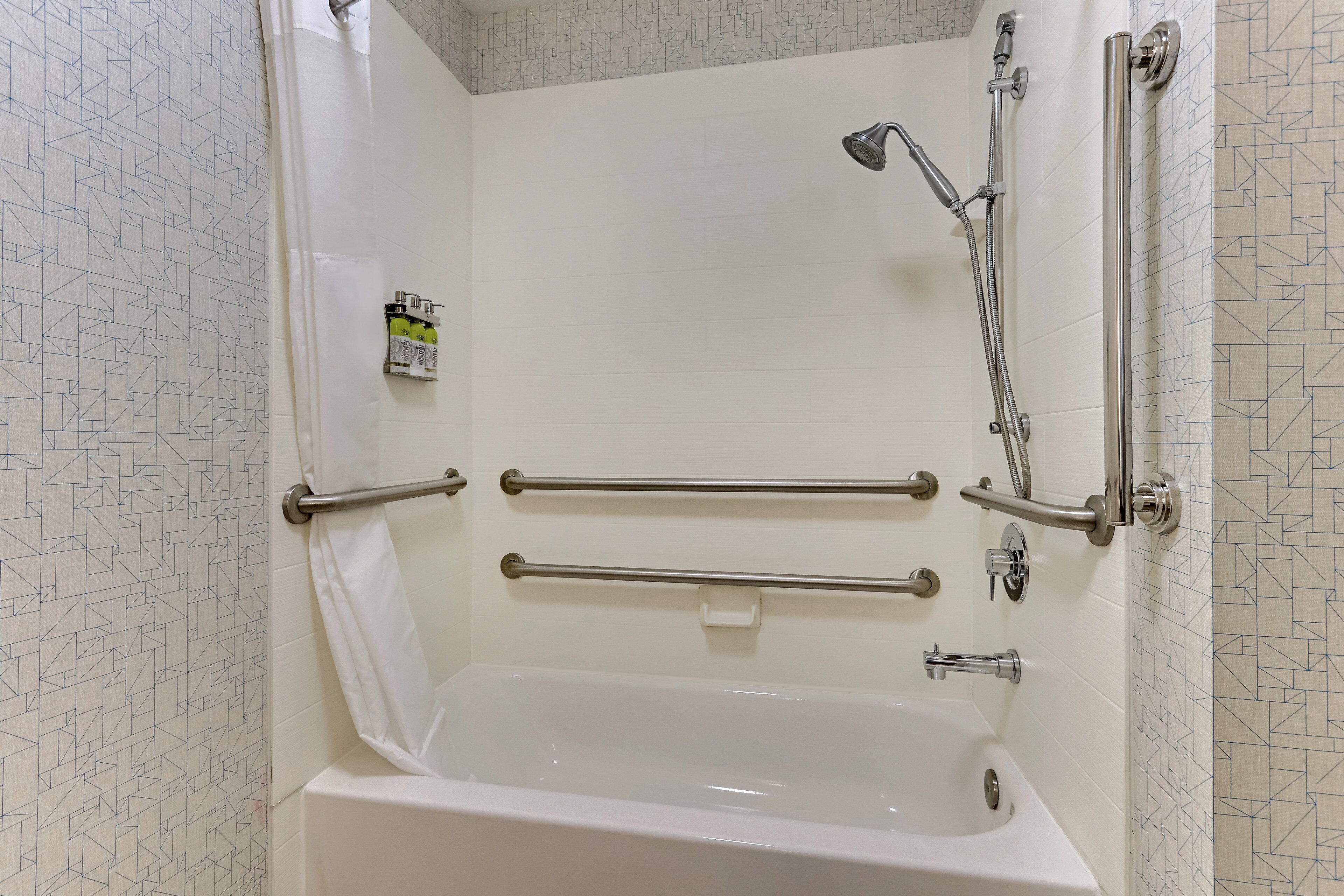 A modern bathroom with a bathtub, grab bars, and a showerhead.