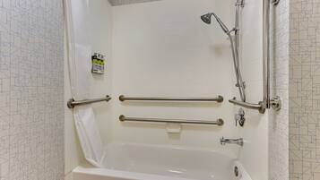 A modern bathroom with a bathtub, grab bars, and a showerhead.
