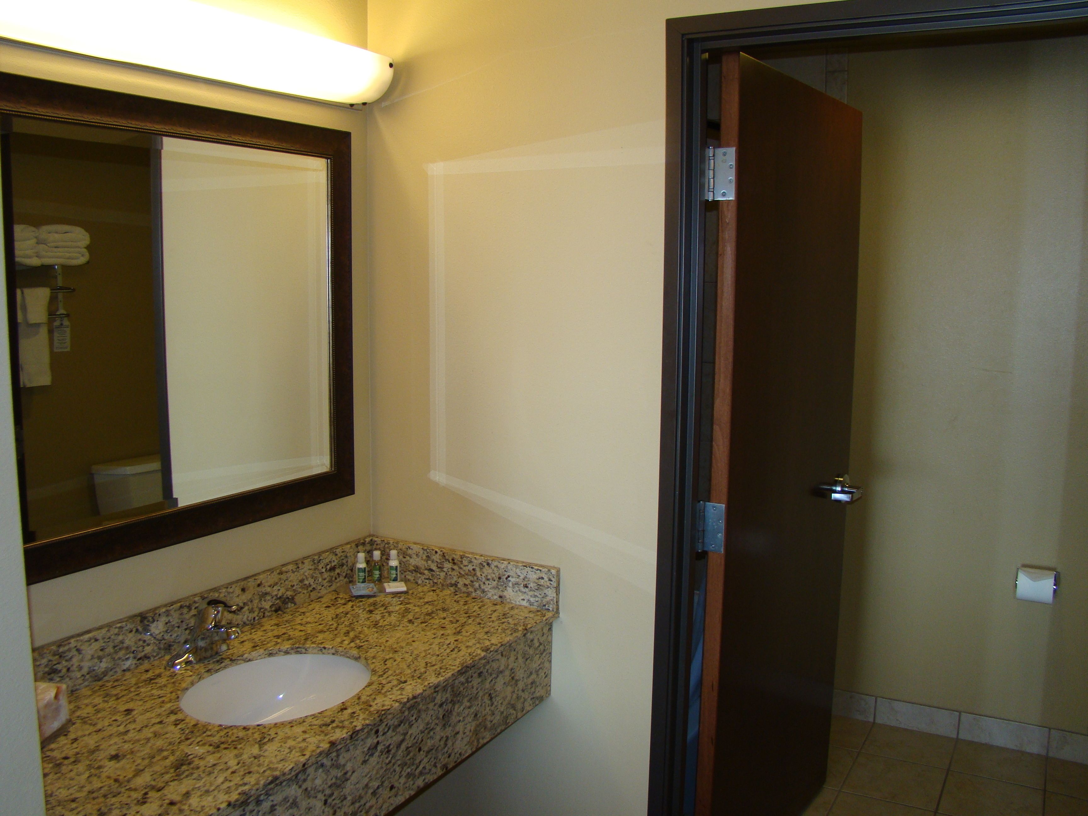 A bathroom with a granite countertop, a sink, a mirror, and a door leading to another room.