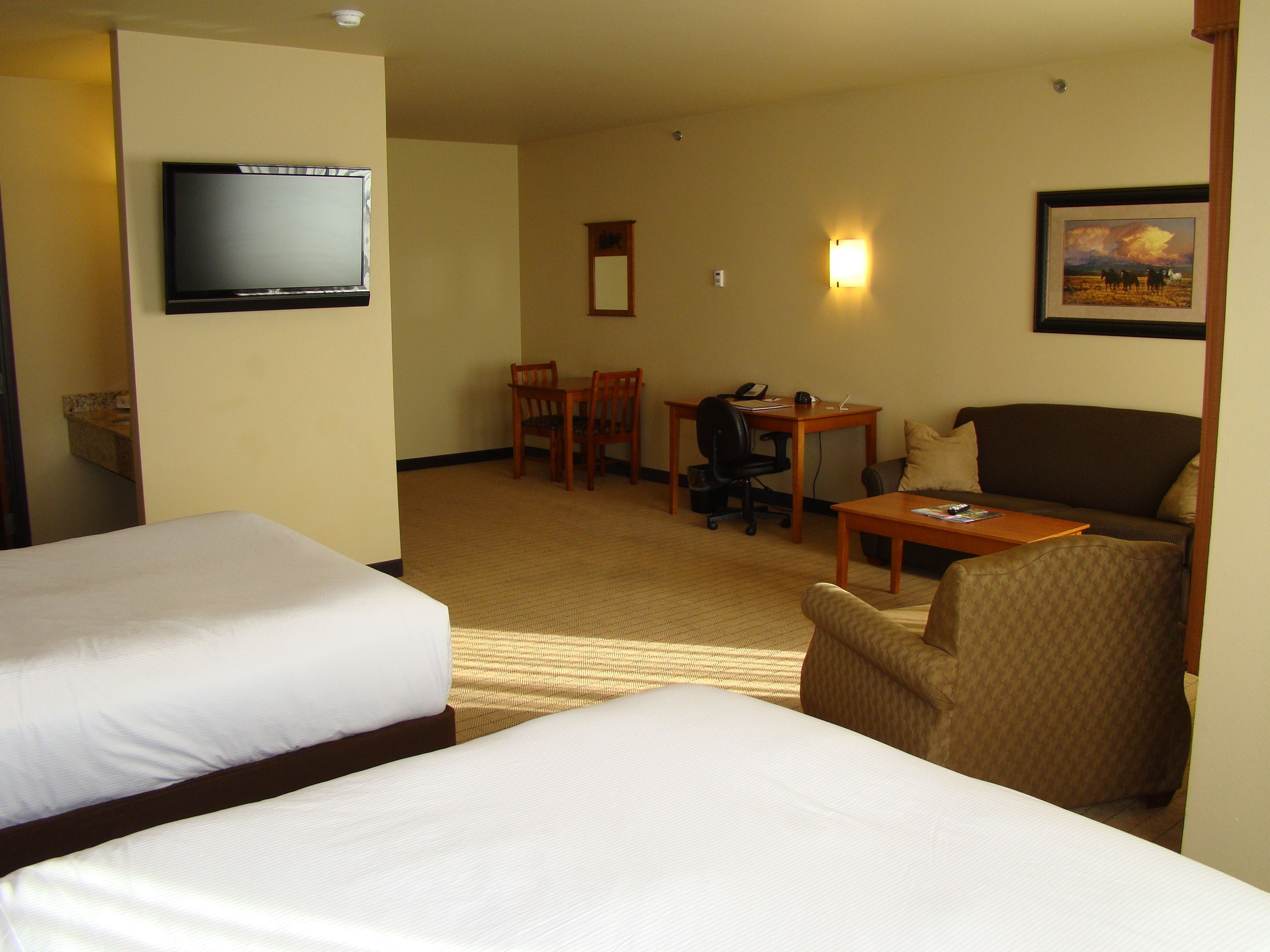 A hotel room with two beds, a desk with a computer, a chair, and a television on the wall.
