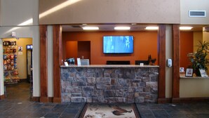 A reception area with a stone counter, a television mounted on the wall, and a small plant on the right. - StoneCreek Lodge (Missoula)
