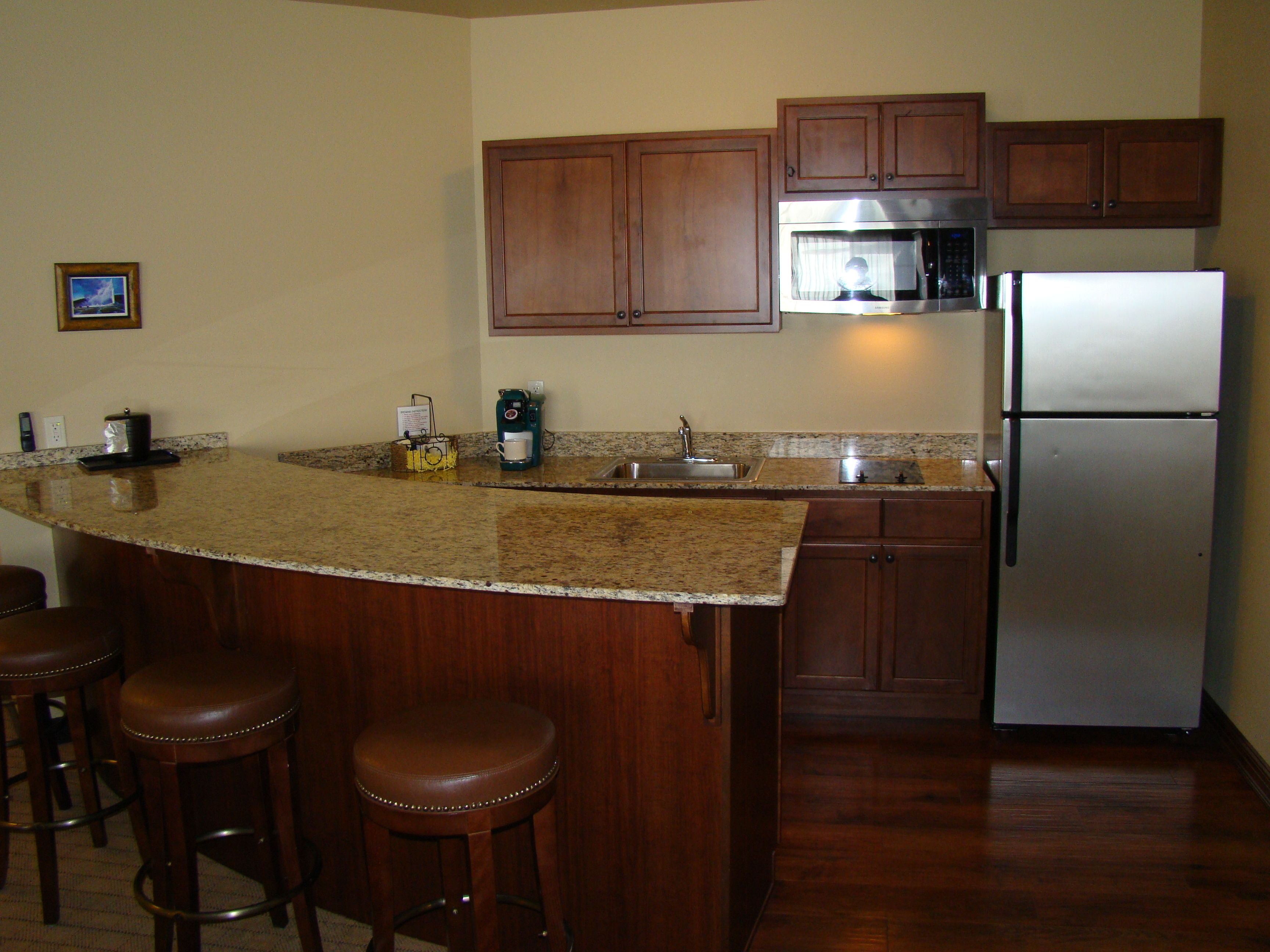 A kitchen with wooden cabinets, a stainless steel refrigerator, a granite countertop, and a coffee maker.