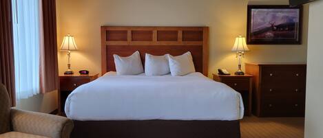 A hotel room with a large bed, two bedside tables with lamps, a chair, a dresser, and a framed picture on the wall.