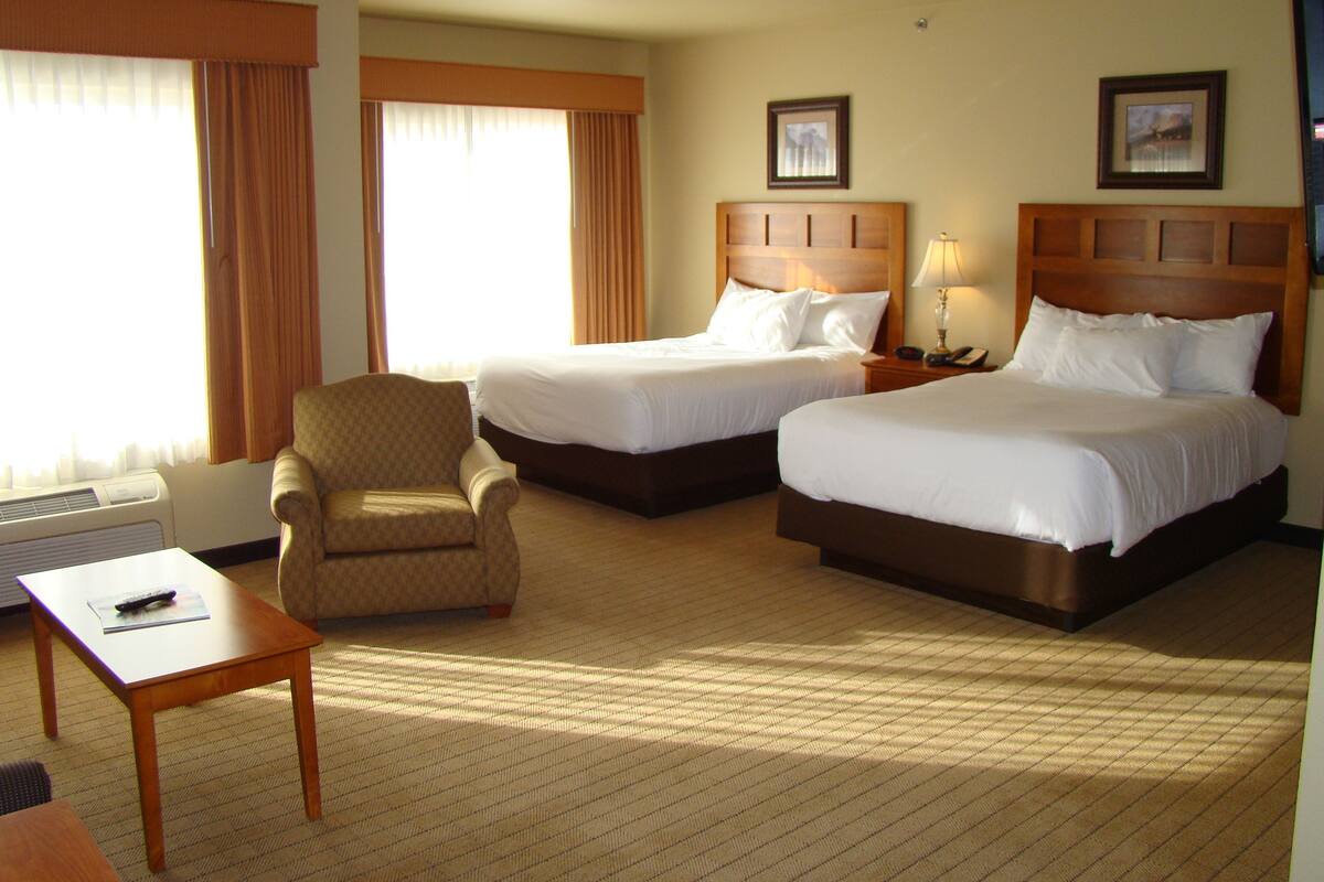 A hotel room with two beds, a chair, a table, and a lamp.