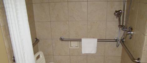 Un espacio de ducha pequeño con azulejos, una barra de apoyo, una silla de ducha blanca y una toalla colgada en la barra.