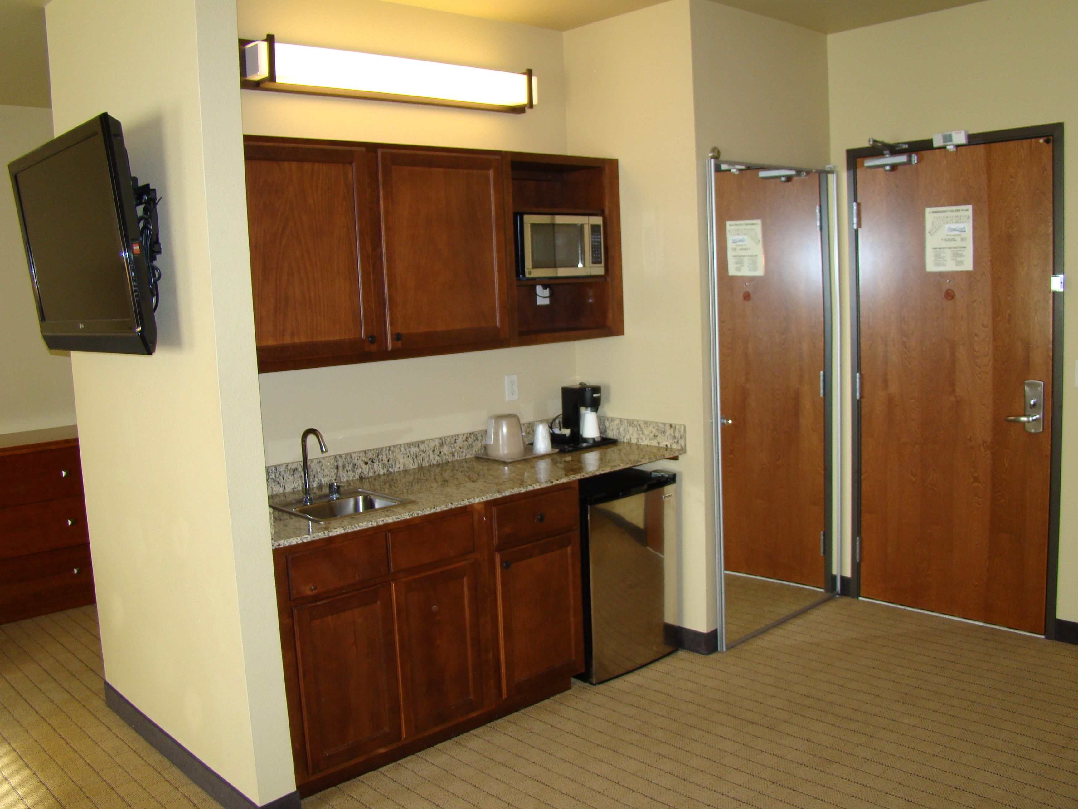 A compact kitchen with wooden cabinets, a microwave, a coffee maker, and a sink.