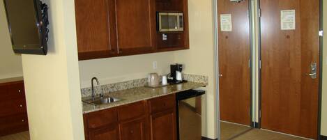 A compact kitchen with wooden cabinets, a microwave, a coffee maker, and a sink.