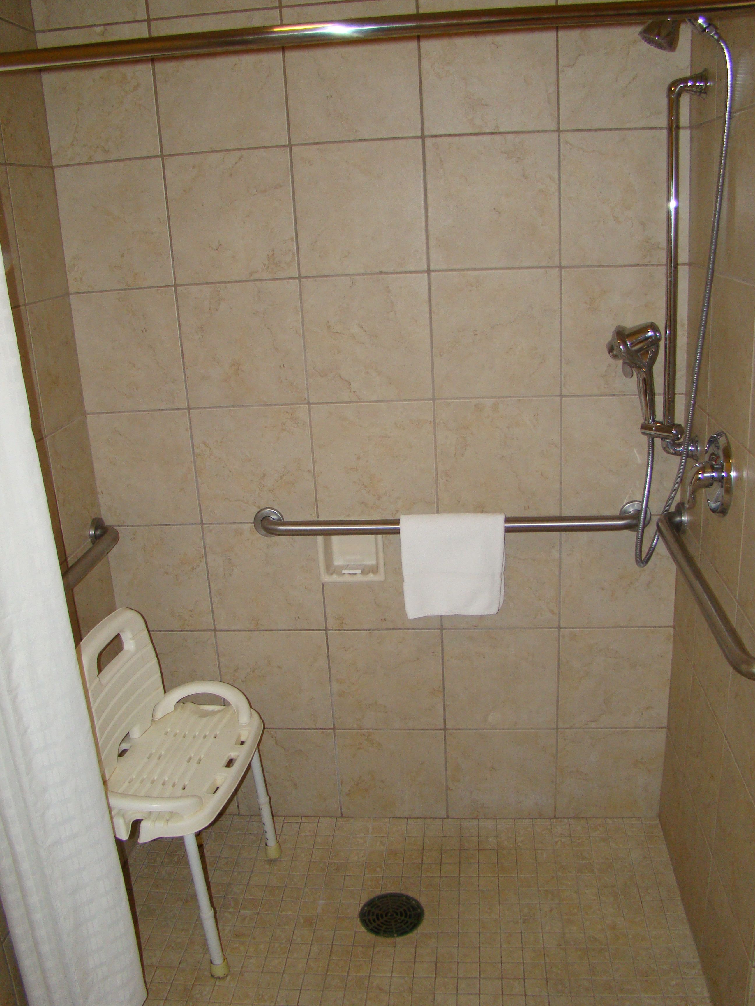 Un espace douche équipé d’une barre d’appui, d’une chaise blanche et d’un porte-serviettes.