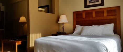 Habitación de hotel con una cama grande, una mesita de noche con lámpara, cabecero de madera y un cuadro en la pared.