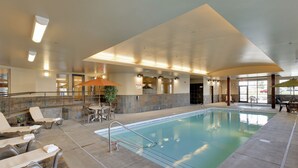 An indoor swimming pool with lounge chairs and a sun umbrella, surrounded by stone walls and a tiled floor. - StoneCreek Lodge (Missoula)