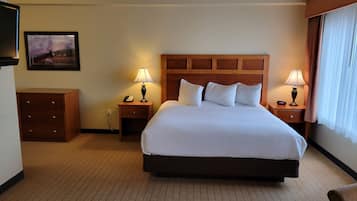 A hotel room with a large bed, two bedside tables with lamps, a wooden headboard, a small wooden dresser, and a framed picture on the wall.
