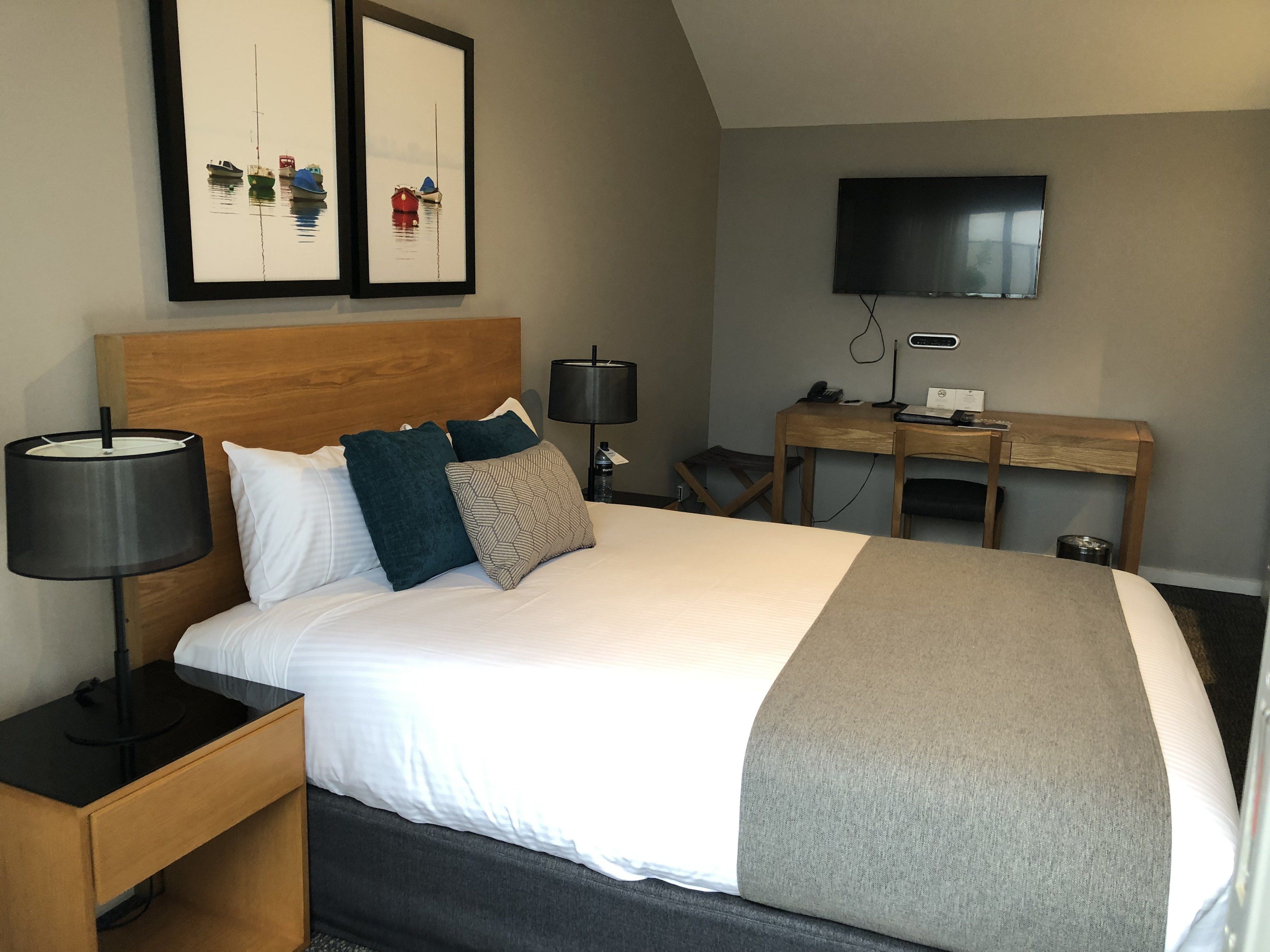 Una camera d'albergo ordinata con un letto grande, una scrivania, una TV e due opere d'arte appese alla parete.