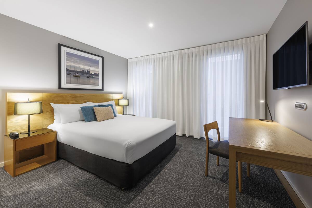 Ett hotellrum med en stor säng, sänglampor, ett skrivbord och en tv.