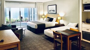 Habitación de hotel con una cama grande, dos mesitas de noche con lámparas, un escritorio pequeño con una silla, un microondas y vistas al exterior a través de amplias ventanas.