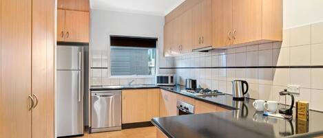 A modern kitchen with wooden cabinets, stainless steel appliances, and a black countertop.