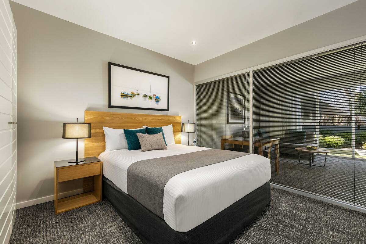 Ett modernt hotellrum med en stor säng, sänglampor, en sänggavel, ett inramat konstverk och utsikt genom fönster som sträcker sig från golv till tak.