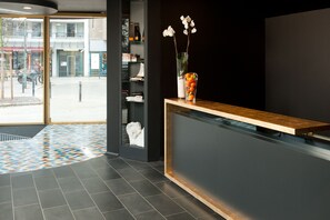 A reception area with a modern design, featuring a reception desk, a glass display case with a vase of flowers, and a patterned floor.