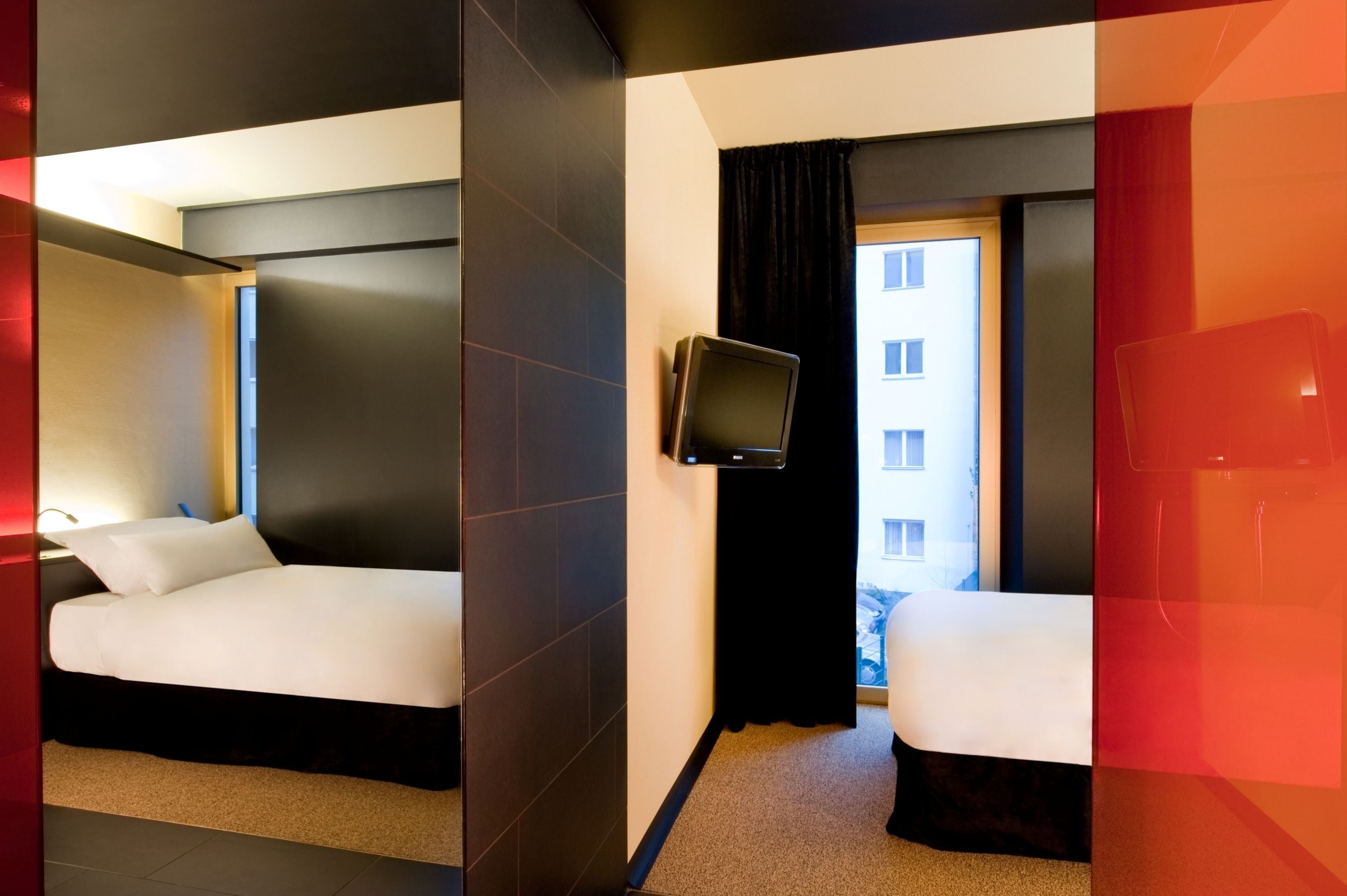 Une chambre d’hôtel avec deux lits, une télévision et une vue sur un bâtiment situé à l’extérieur.
