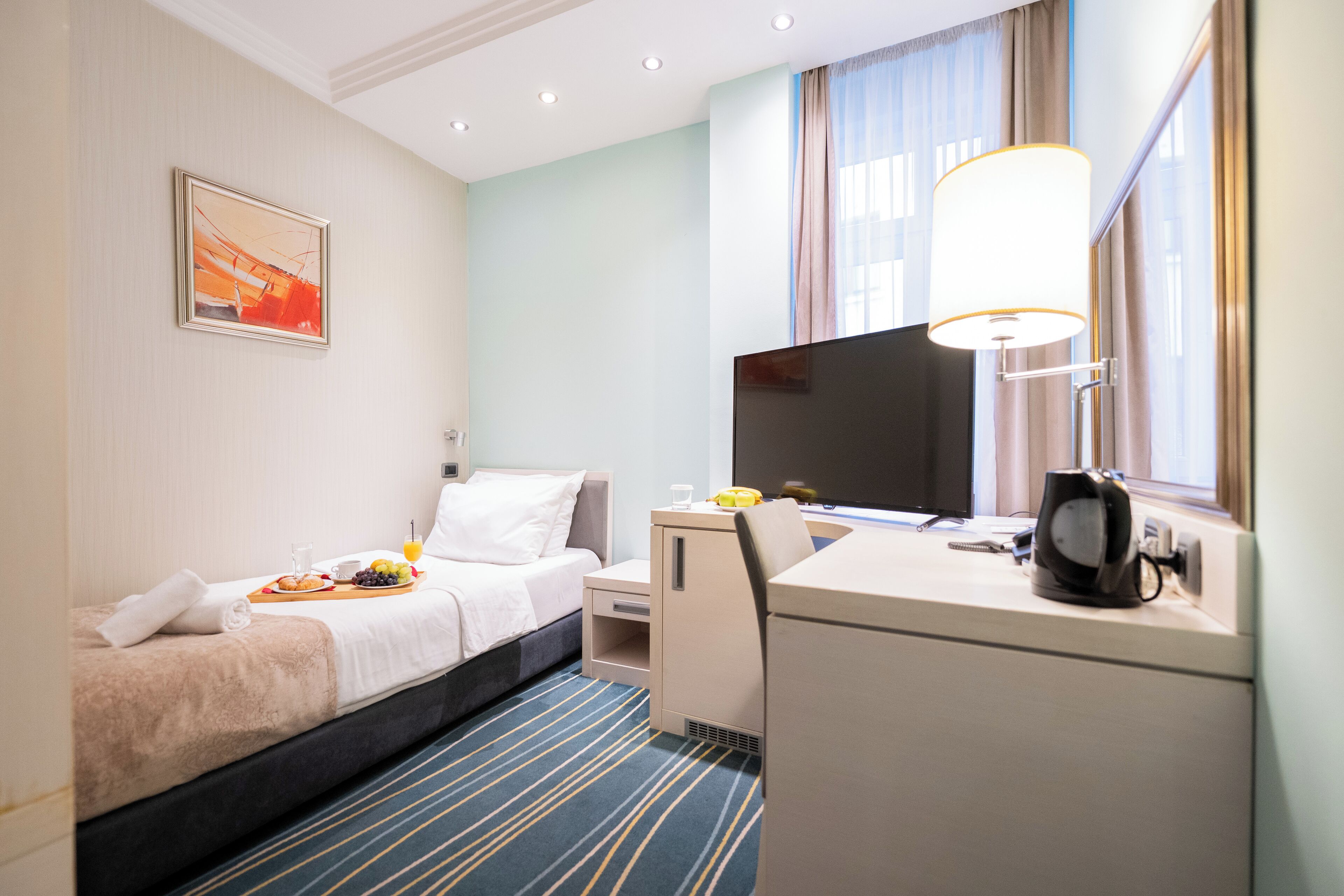 A hotel room with a bed, a desk, a TV, and a window with curtains.
