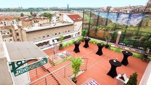 Una terraza en la azotea con asientos al aire libre, vista del paisaje urbano y una pantalla grande mostrando un paisaje.