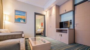Habitación de hotel con sofá, mesa de centro de vidrio, televisor y armario.