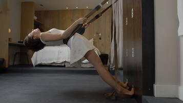 A person performing a yoga pose in a room with a bed, wooden panel walls, and a dark floor.