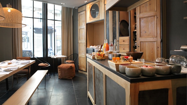 A modern kitchen with wooden cabinets, a central island with bowls, and a dining area with a bench and chairs. - Hidden Hotel (Paris)