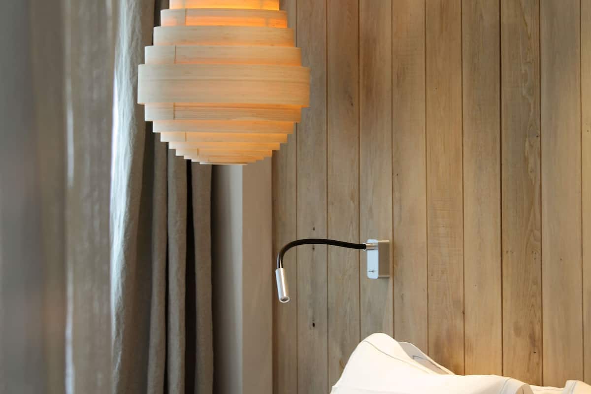 Une chambre avec un mur en bois, un luminaire suspendu et un lit recouvert de linge de lit blanc.