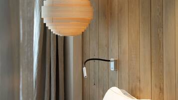 A bedroom with a wooden wall, a hanging light fixture, and a bed with white bedding.