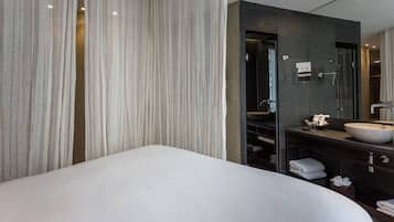 Een moderne hotelkamer met een groot bed, een donkere badkamermeubel en een grote spiegel.