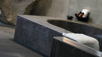 Une salle de bain moderne avec un grand élément décoratif en pierre, un lavabo intégré et une cloison en verre.