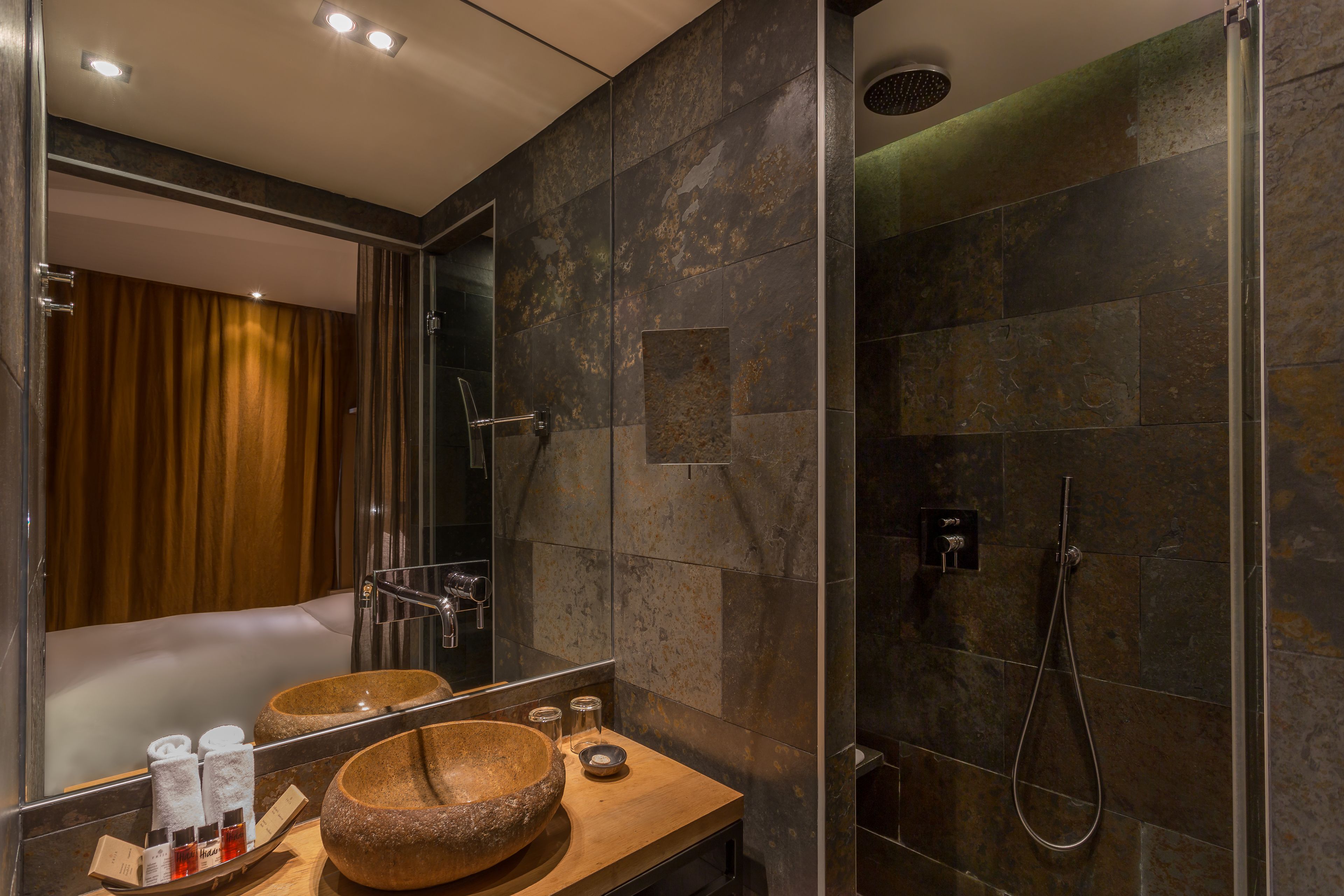 Une salle de bain moderne avec un grand miroir, un meuble-lavabo en bois, un vasque en pierre et une douche à parois de verre.